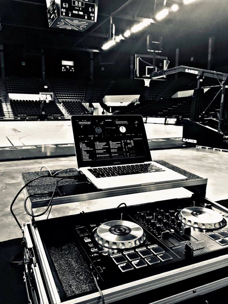 A DJ controller and laptop set up courtside in an empty arena before an event.